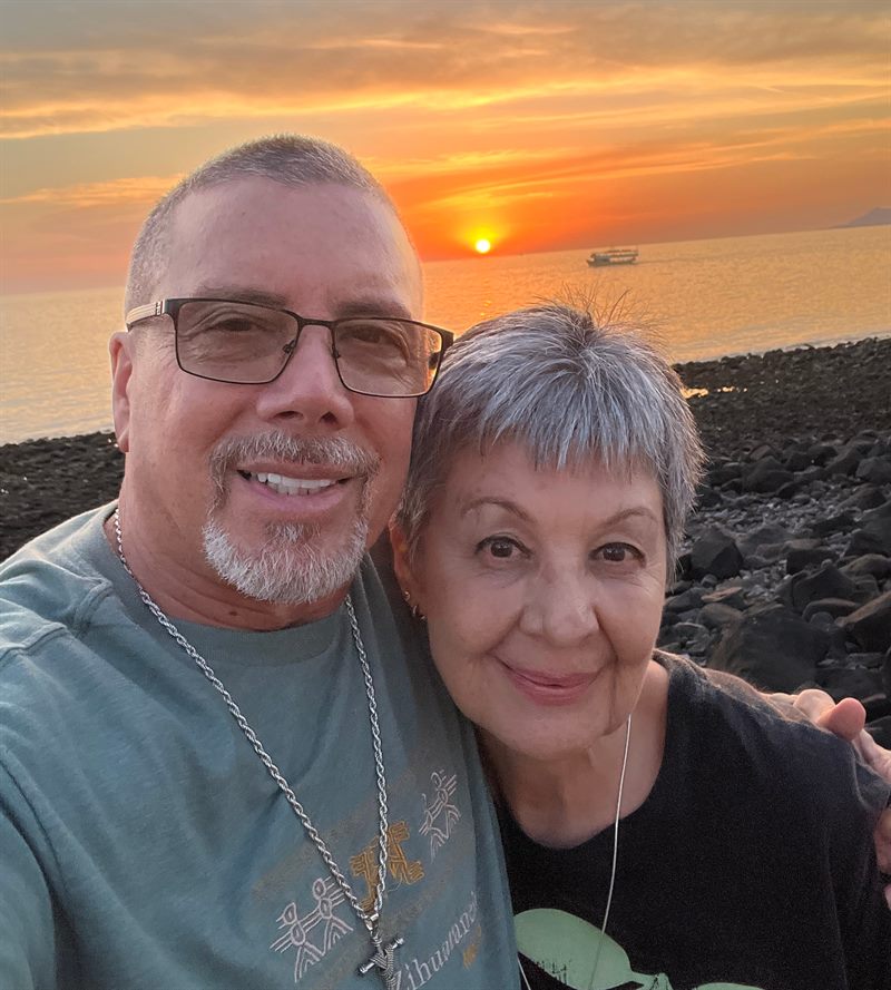 Abel Gaxiola and his wife smiling on a rocky beach at sunset
